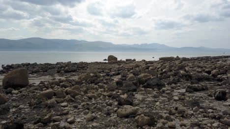 Strange-creepy-Martian-mountain-range-rocky-alien-stone-beach-coastline-descend-low-reverse