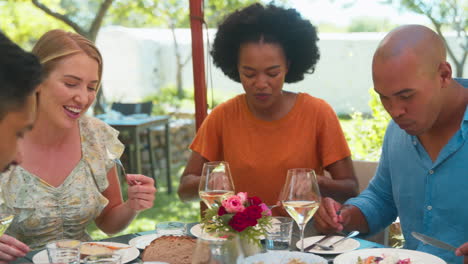 group of friends enjoying outdoor meal and wine on visit to vineyard restaurant