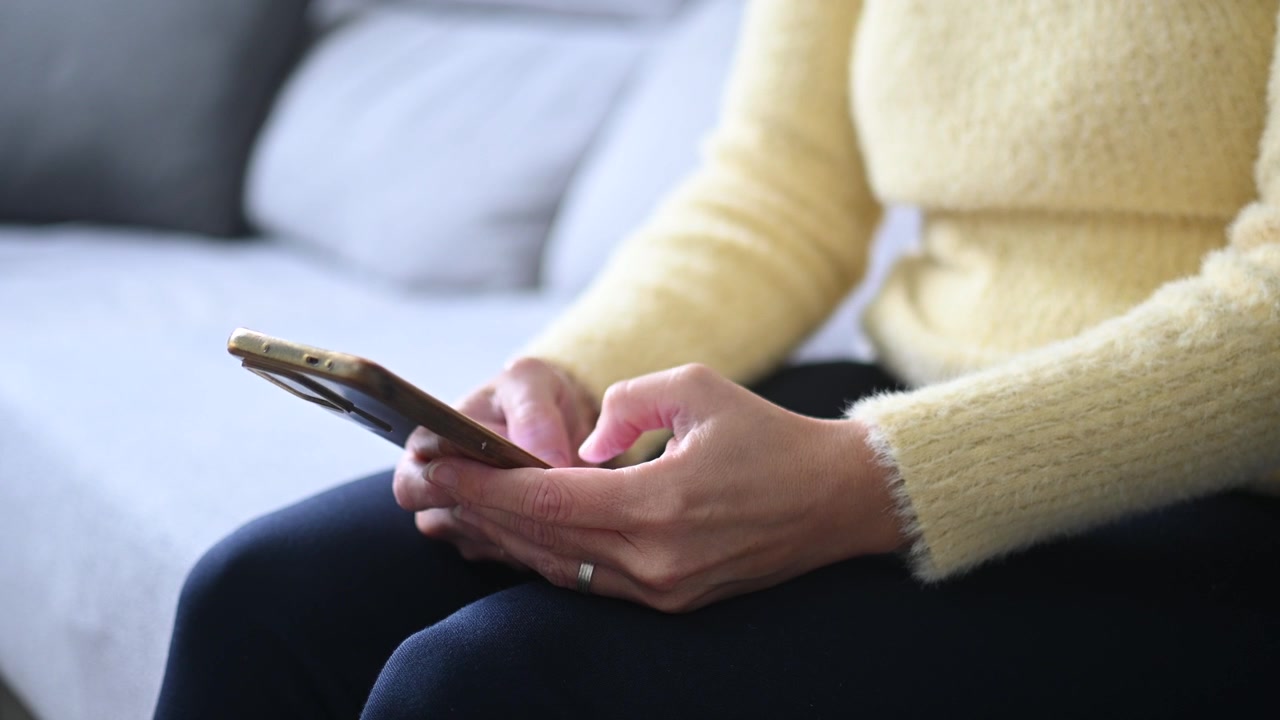 Primo piano di una donna che digita sullo smartphone a casa.