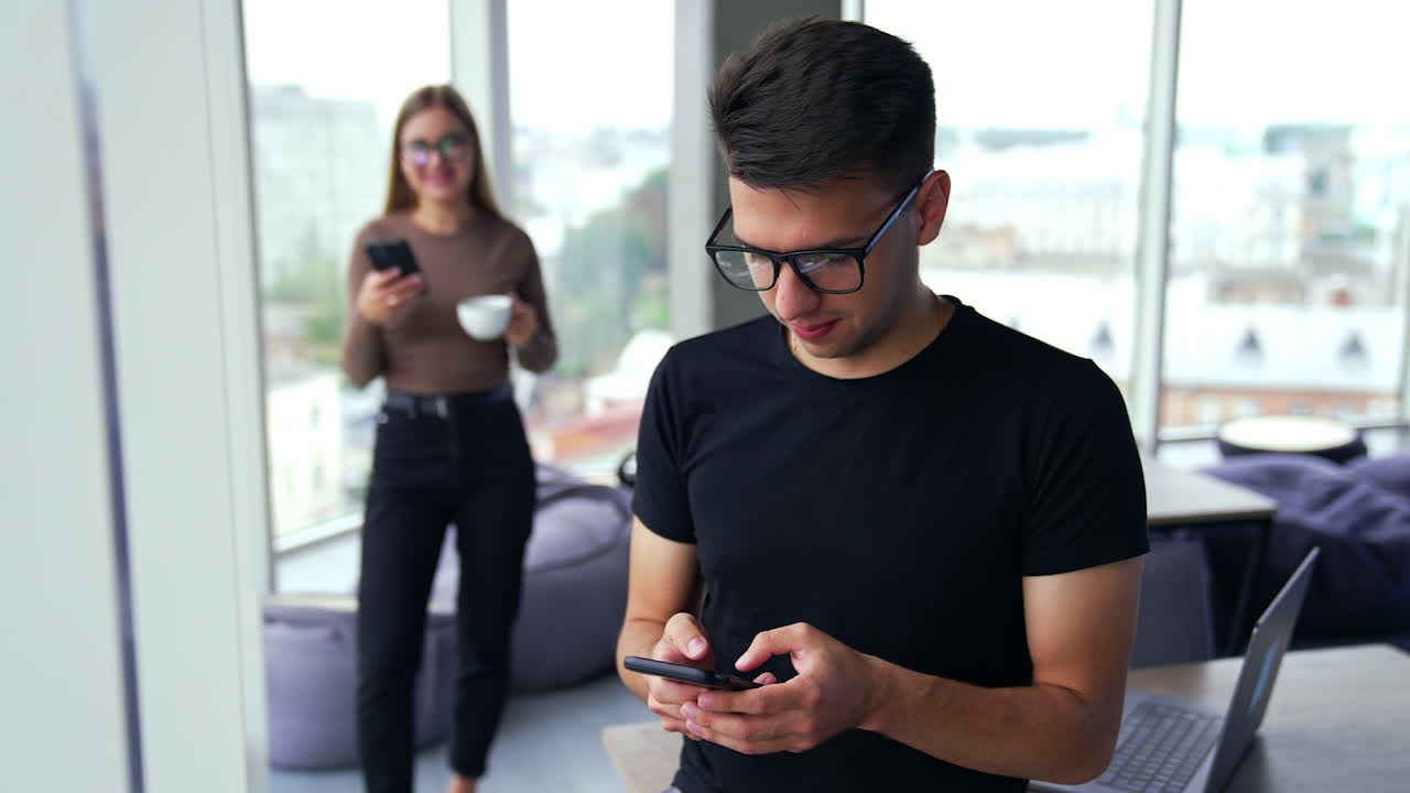 Lunch time in spacious office. People standing in the room using their phones, drinking coffee. Blurred panoramic window at backdrop.