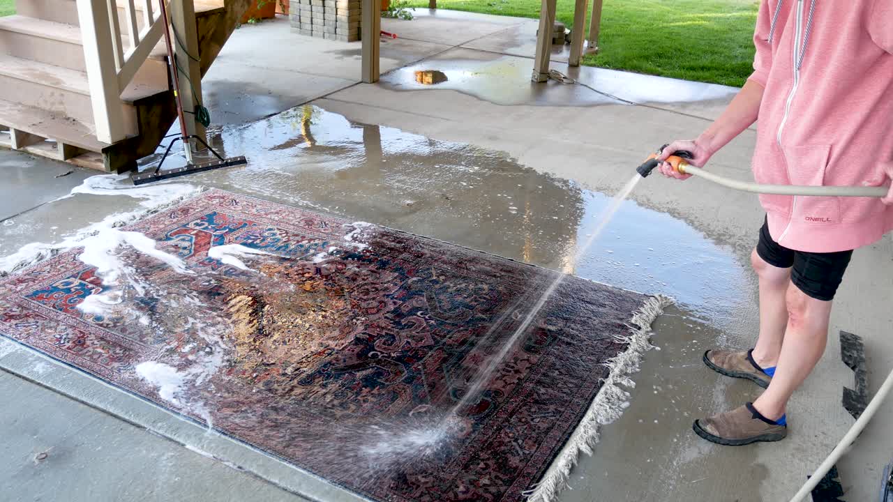 usando una manguera para rociar el jabón de una alfombra oriental recién limpiada - toma panorámica