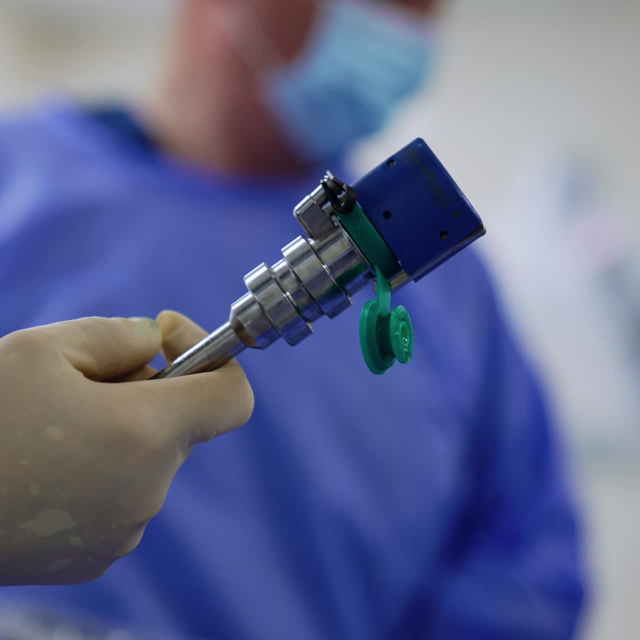 Gloved doctor's hand hold the piece of robotic equipment. Another doctor in mask stands at backdrop in blur