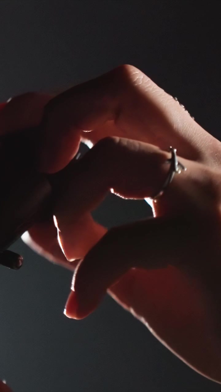 Female adult fingers clutch tiny metallic cylinders. Two sets of hands position cylindrical shapes revealing. Cylindrical items are held against simple unadorned backdrop