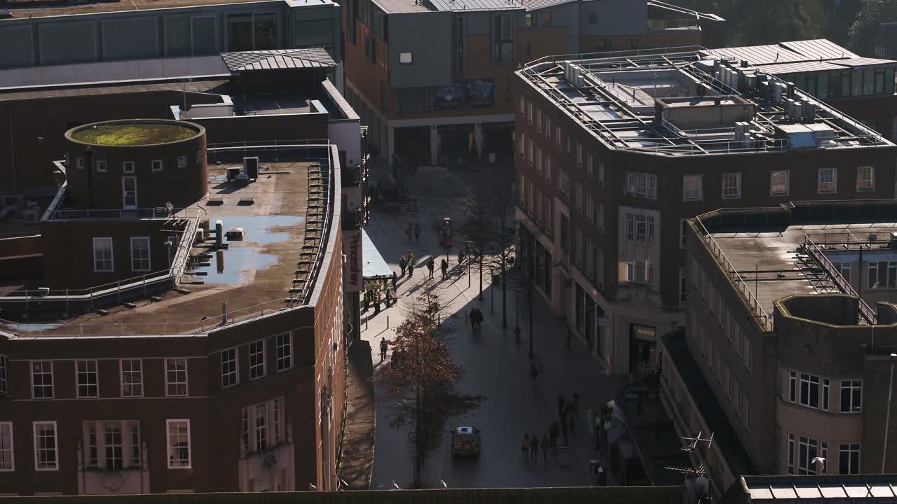 Aerial of a busy shopping street in the UK. The drone flies over buildings to reveal the modern shaded street