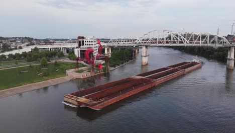 spectacular view of tugboat guiding large commercial transport barge down river beneath truss bridge, illinois, aerial