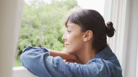 happy caucasian woman looking through window and wearing jacket in living room