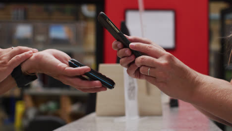 Midsection-of-caucasian-woman-making-contactless-phone-payment-over-the-counter-at-gym