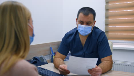 male obstetrician in mask and blue uniform consulting the patient. doctor listens to patient's complaints and nods.