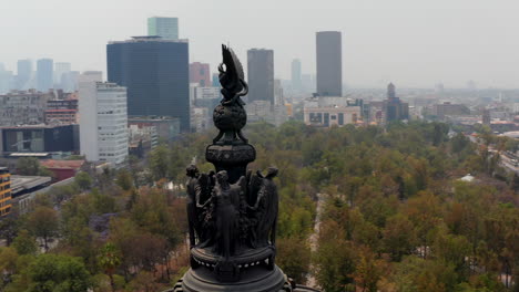 Drohne,-Die-Um-Statuen-Auf-Dem-Denkmal-Herumfliegt,-Das-Sich-Auf-Einer-Hohen-Säule-Befindet.-Kreisförmige-Ansicht-Von-Figuren-Und-Mexiko-stadtpanorama.-Bauvielfalt-In-Der-Stadt.