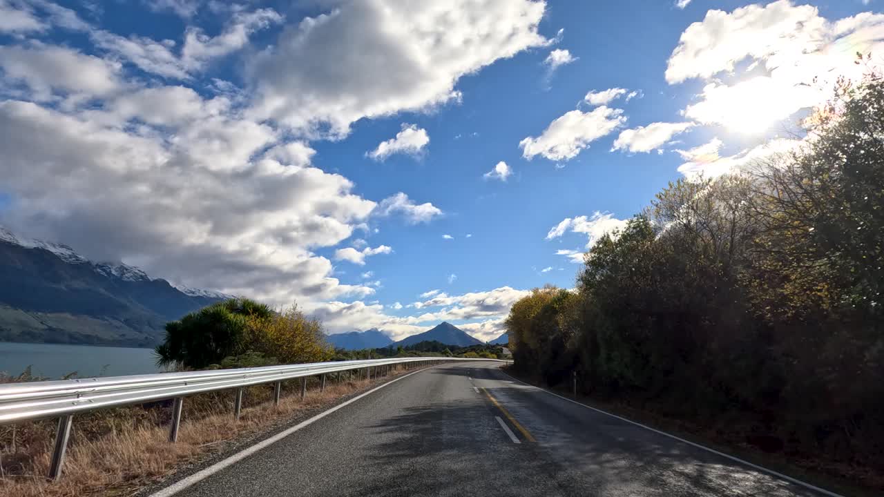 Point-of-view drive on winding lakeside road, mountains, dramatic clouds, daylight, smooth camera movement