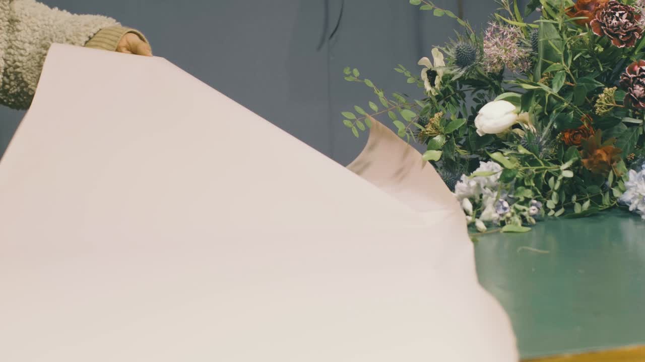 a florist prepares a bouquet of flowers, cuts paper and wraps the flowers into a beautiful arrangement