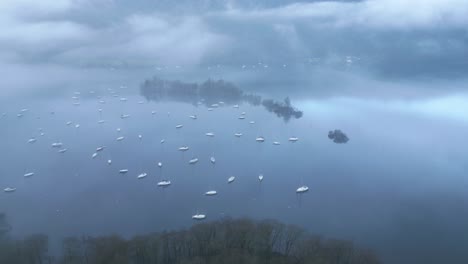 retreating drone shot of the windermere lake, showing the sailboats sailing and floating in the waters of the lake district of cumbria in england