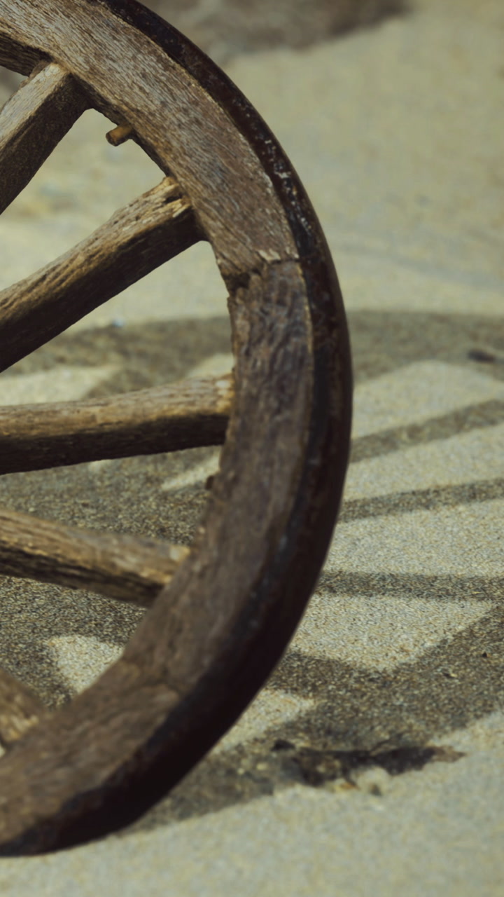 Wooden wheel on sandy ground at a rural location during daylight