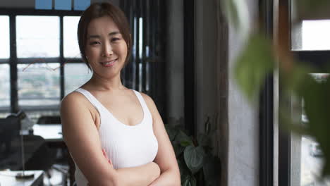 asian woman standing by window in business office, arms crossed, looking confident, copy space