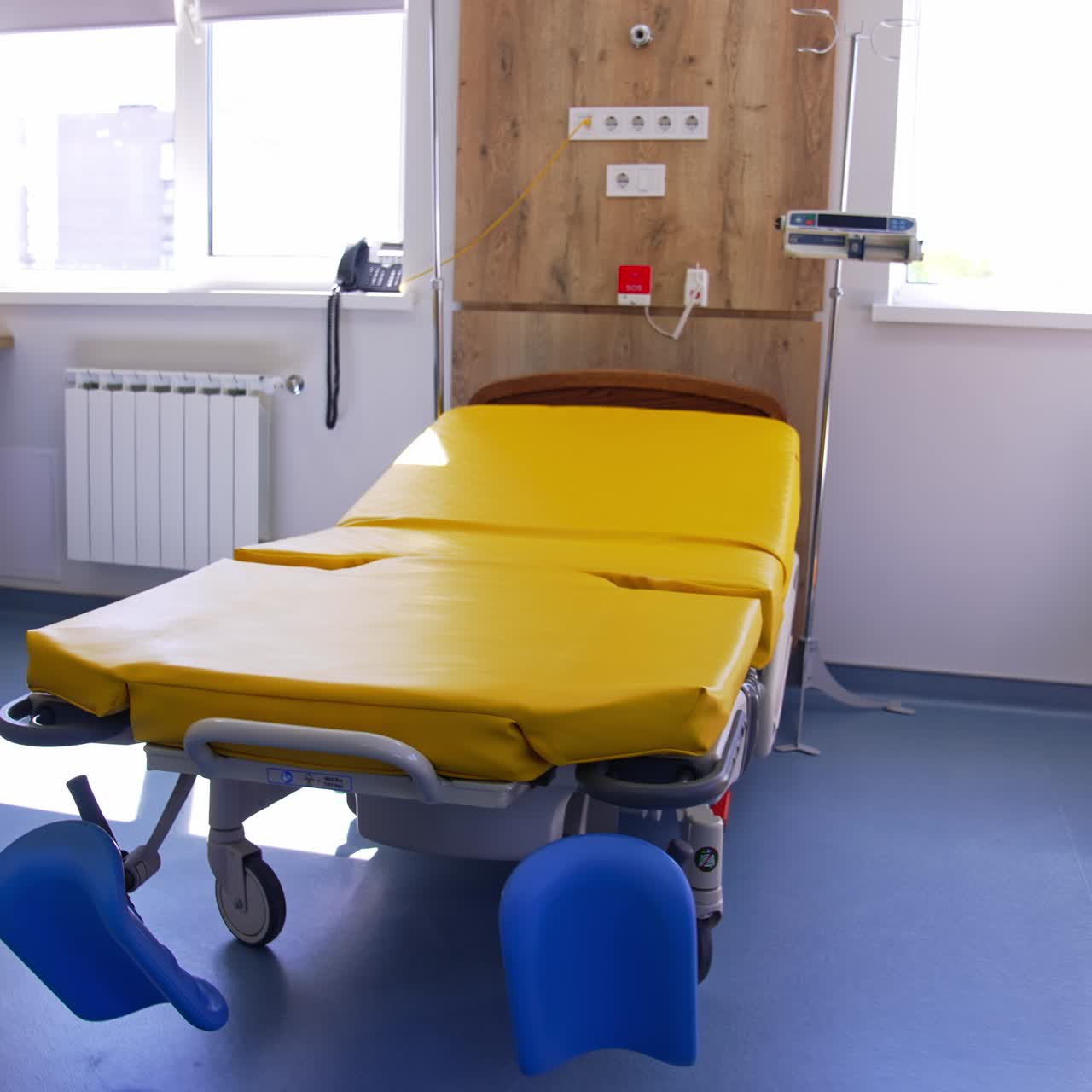 New light ward with empty yellow bright bed for ladies in labor. Comfortable furniture and advanced equipment on both sides of the bed