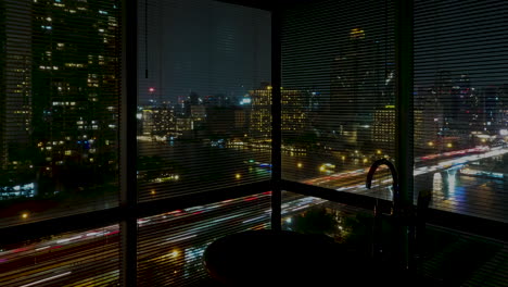 Bathroom-view-with-big-windows-with-blinds-and-bathtub-on-a-night-timelapse-modern-city-of-Bangkok-with-traffic-and-boats-on-the-river