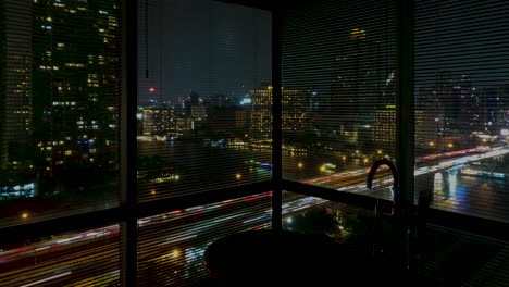 bathroom view with big windows with blinds and bathtub on a night timelapse modern city of bangkok with traffic and boats on the river