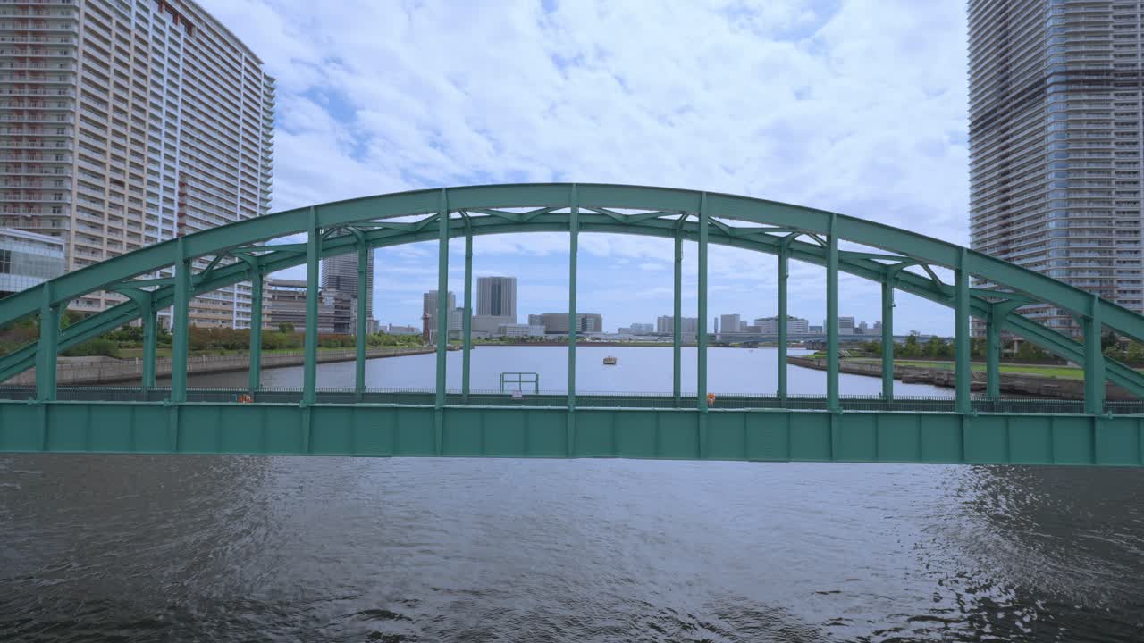A shot of the old Harumi Railway Bridge, with its green metal arch, connecting the city's modern buildings