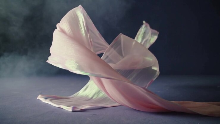 Wind lifting iridescent pink ribbon, twisting and rising on studio table for visual effect