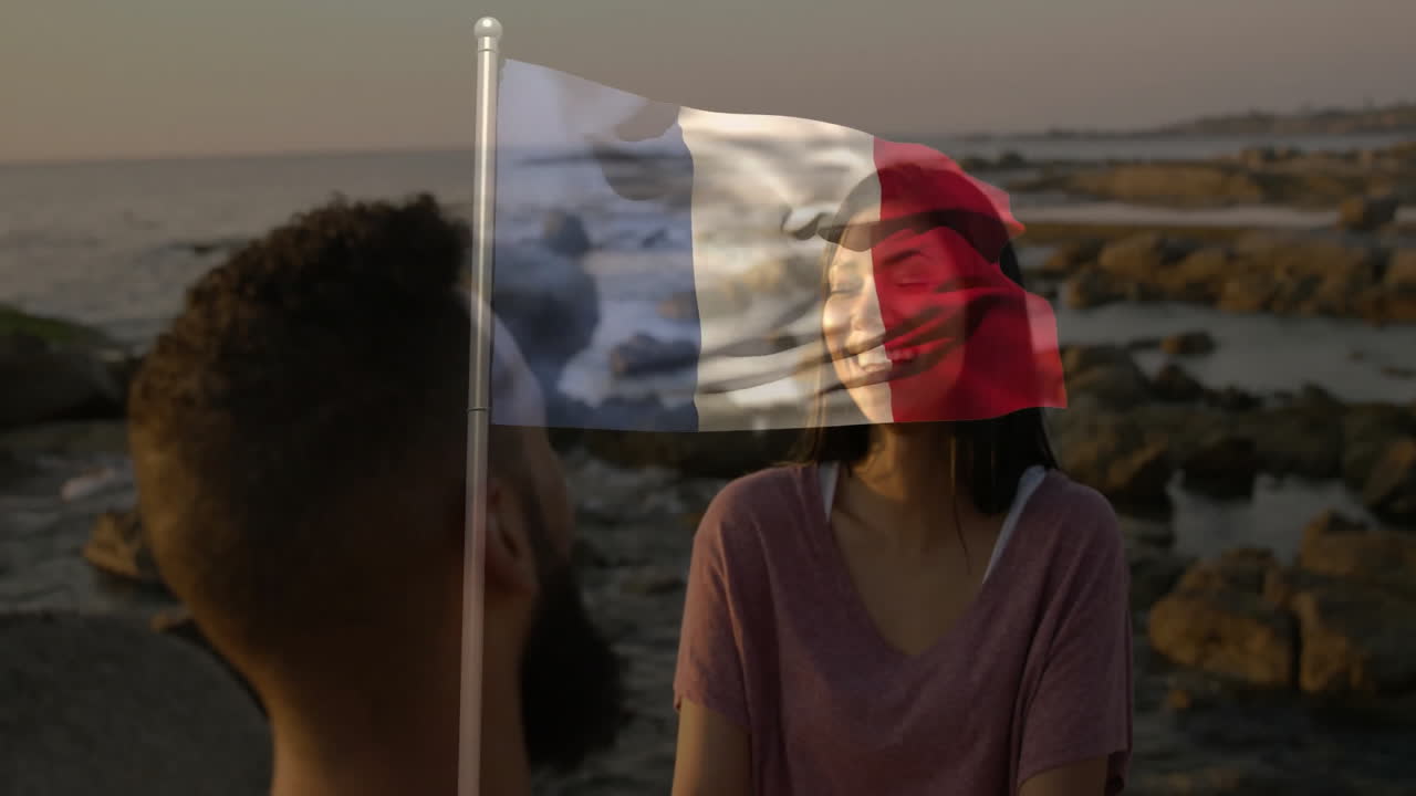 Coppia sorridente in spiaggia con un'animazione in sovrimpressione della bandiera francese in primo piano.