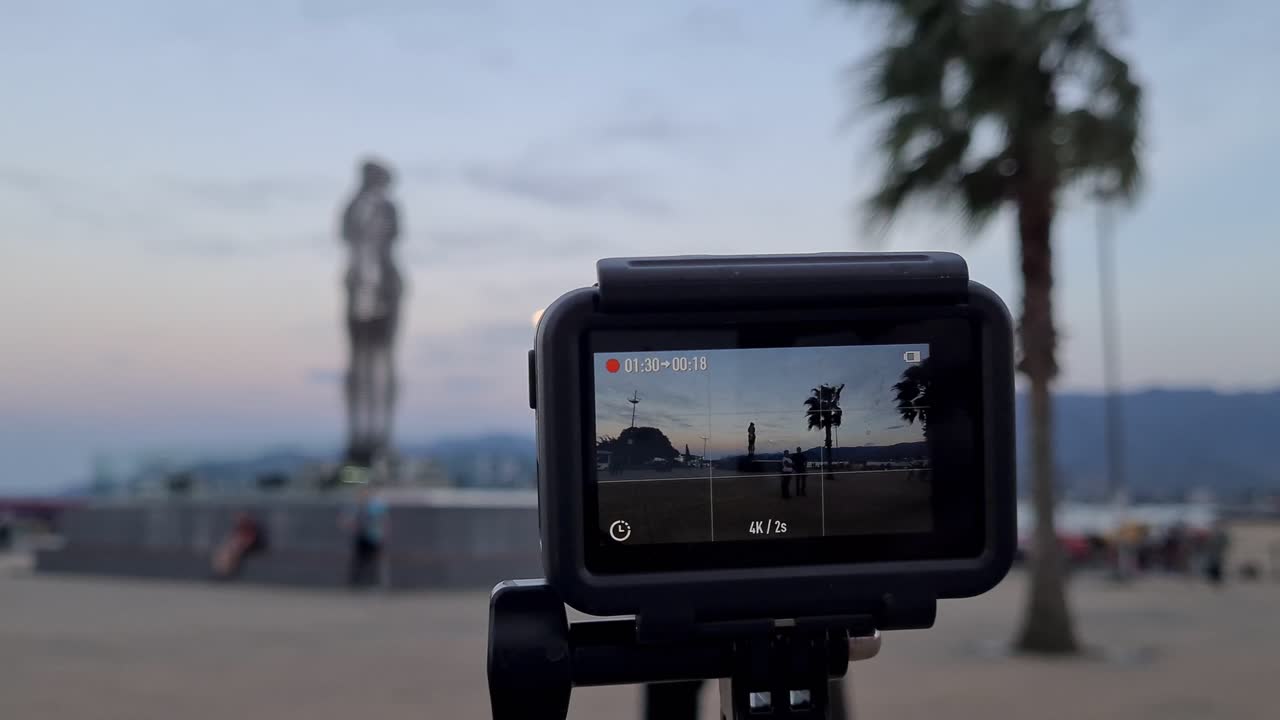 Action camera is taking time laps of Ali and nino statue after sunset. Toursist walk around.