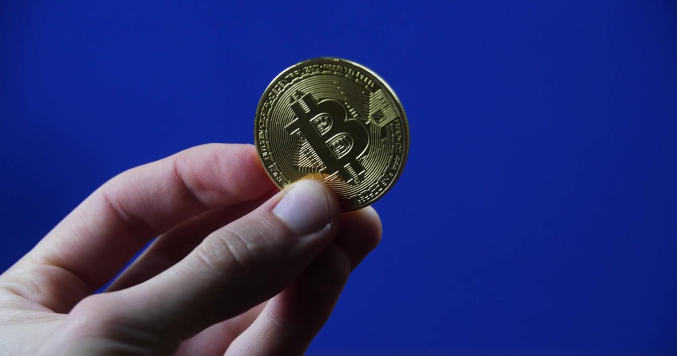 Bitcoin fisico tenuto contro uno sfondo blu chromakey per temi digitali e cripto, ruotato fronte e retro