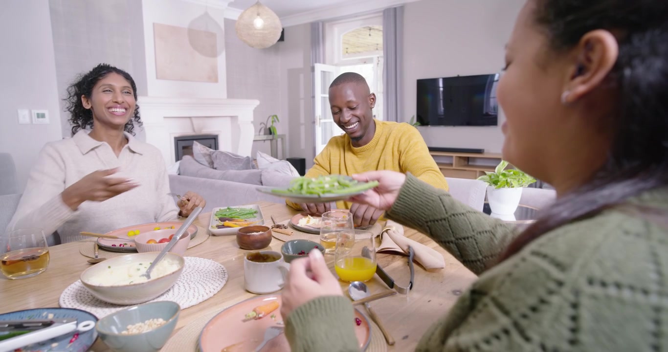 Amigos afroamericanos sirviendo una comida en casa, el hombre con suéter amarillo alcanzando y ofreciendo judías verdes
