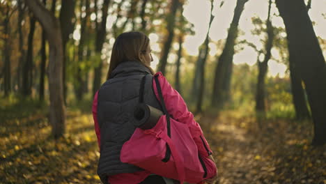 woman walking with yoga mat and bag on an autumn path