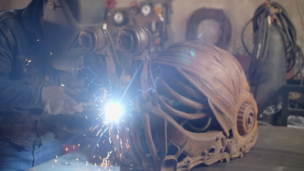 защитник сварит декоративную металлическую скульптуру улитки с большим количеством искр и вспышек в замедленном движении, металлообработка в мастерской, 4k 60p prores hq