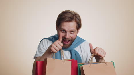 shopaholic man showing shopping bags, advertising discounts, smiling looking amazed with low prices