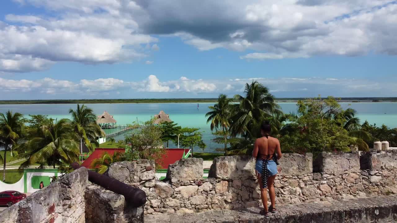 joven viajera caminando dentro del castillo de san felipe en bacalar méxico drone revelando playa tropical con resort de lujo en la laguna del lago azul estado de quintana roo