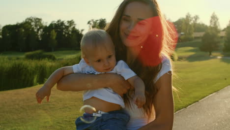 Mujer-Sosteniendo-Al-Niño-En-Las-Manos-En-El-Parque.-Hermosa-Madre-Abrazando-A-Su-Hijo-En-La-Pradera