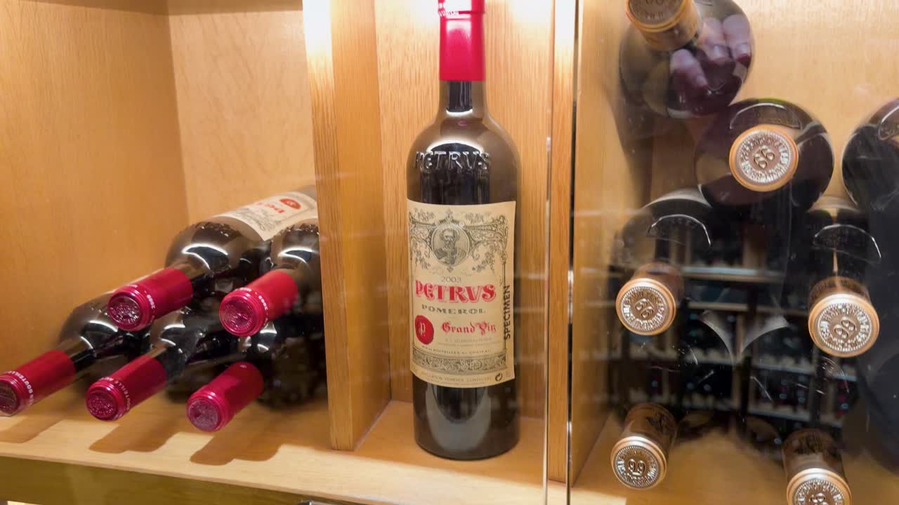 Una cámara en primer plano se desplaza por botellas de vino tinto premium almacenadas en un armario de bodega de madera.