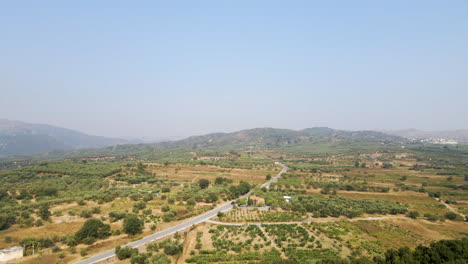 Vista-Panorámica-De-Una-Carretera-En-Un-Terreno-Tupido-Con-Un-Coche-Que-Viaja-Durante-El-Día-En-La-Isla-De-Creta,-Grecia