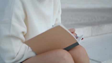 unknown woman writing notebook sitting staircase close up. hands making notes.