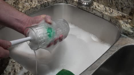 a man scrubs a cup in a foam bubble-filled stainless steel sink