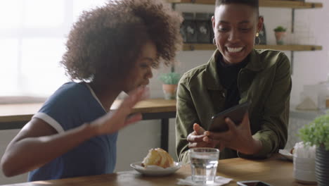 Fröhliche-Afroamerikanische-Frau,-Die-Einen-Tablet-Computer-Benutzt-Und-Einen-Freund-Zeigt,-Der-Zusammen-Lacht-Und-Lustige-Unterhaltung-Auf-Dem-Bildschirm-Eines-Mobilgeräts-Im-Café-Genießt