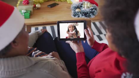madre y hija afroamericanas usando una tableta para una videollamada de navidad con una mujer en la pantalla
