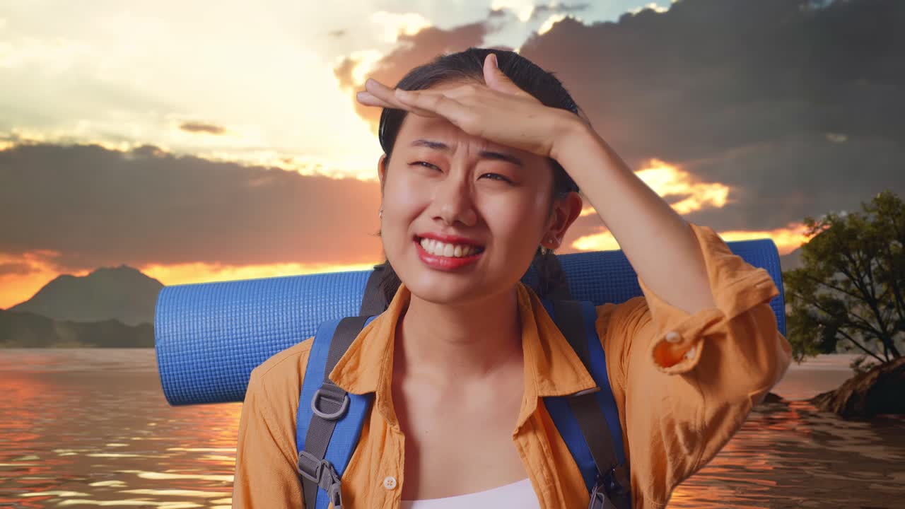 Close Up Of Asian Female Hiker With Mountaineering Backpack Hand Forehead Smiling And Looking Distance While Standing At A Lake During Sunset Time