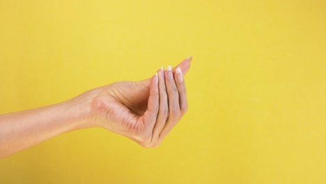 frotando los dedos mostrando el gesto de efectivo pidiendo dinero. cerca de la mano de la mujer aislada en fondo amarillo