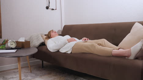 patient lies on brown sofa gazing upward while speaking with emotional coach during reflective session, tissue box, notebook, pencils and clock rest on table adding to calm therapeutic atmosphere