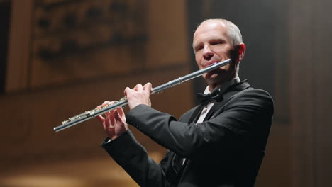 aged flutist is playing neoclassic music by flute portrait of musician in concert hall of philharmonic