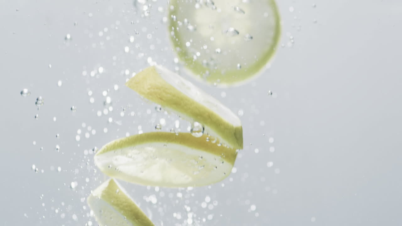 백색 배경에 복사 공간과 함께 물에 떨어지는 라임과 레몬 조각의 비디오