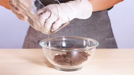 manos con guantes verter fichas de chocolate en un cuenco de vidrio