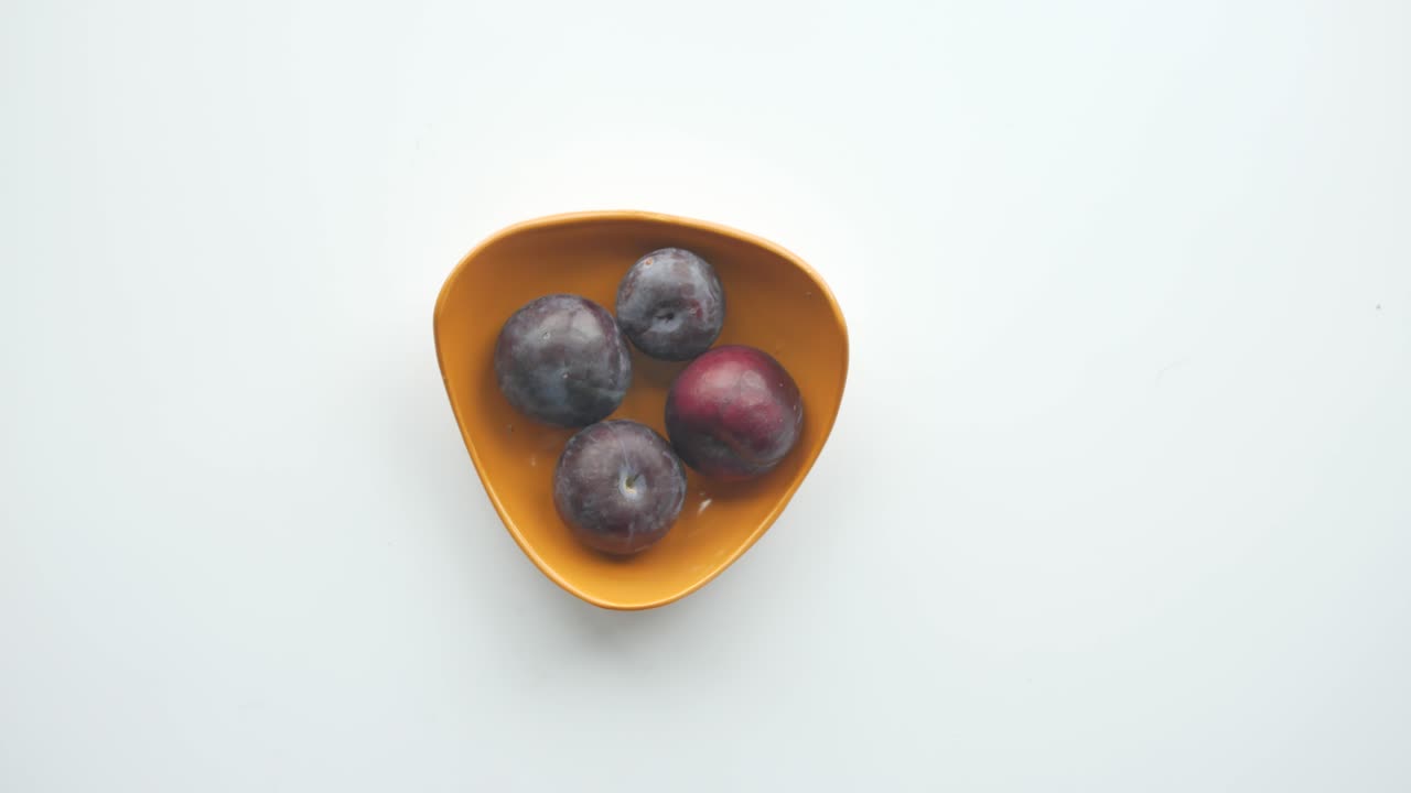 Hand picking a plum from a bowl of plums
