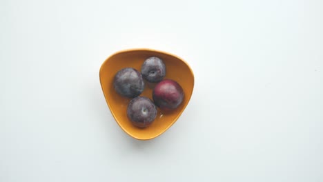 hand picking a plum from a bowl of plums