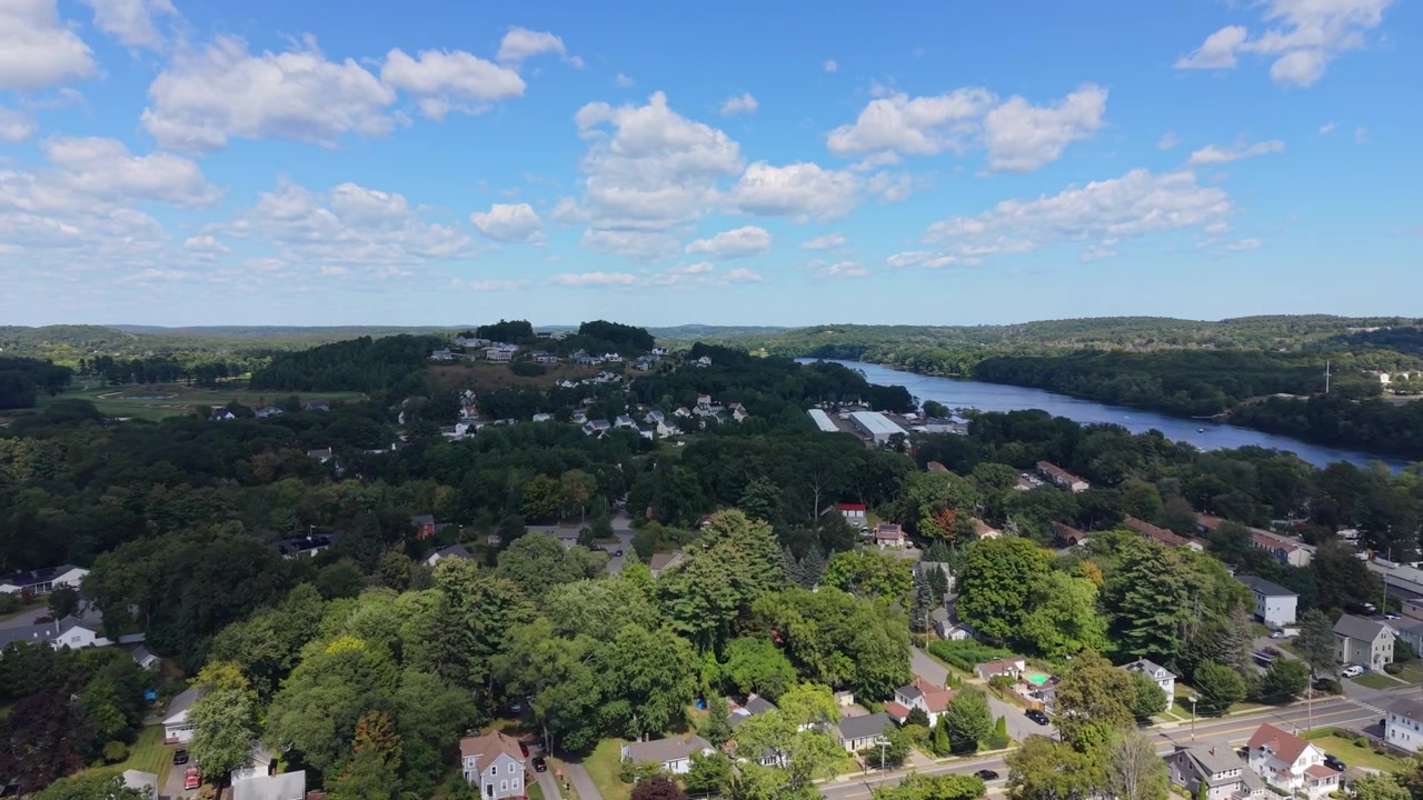 Drone flying forward over the houses, main road and traffic of Haverhill, Massachusetts toward the Merrimack River and rolling wooded hills on a clear afternoon.