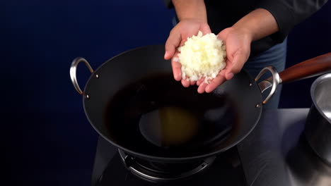 adding chopped onions to a wok