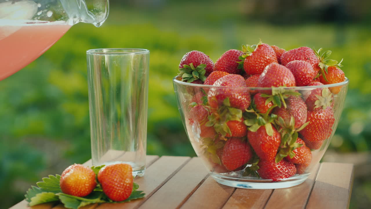 Versare il succo in un bicchiere accanto a un piatto di fragole fresche 1