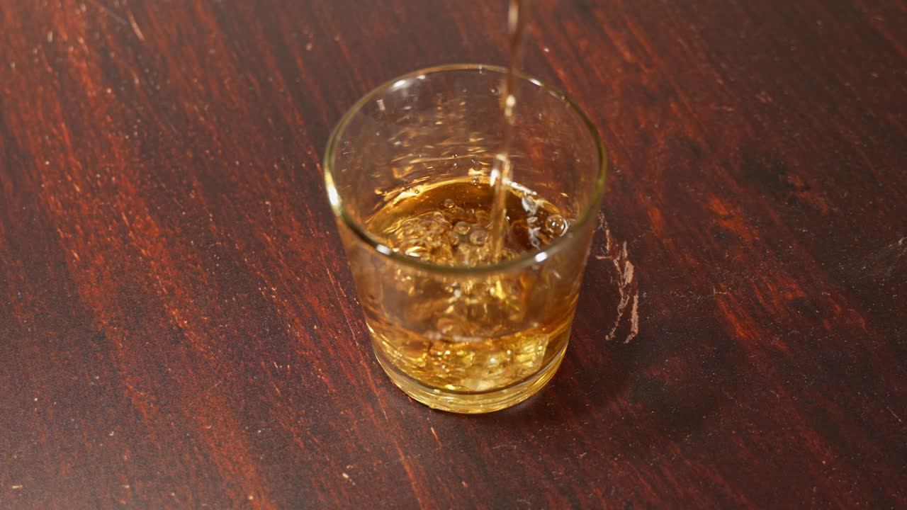Slow motion view of golden whiskey flowing smoothly into a clear glass on a table, capturing the warmth and richness of the spirit